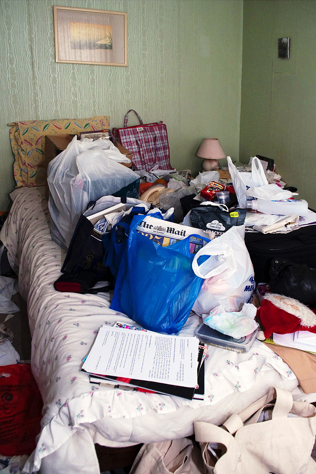 Bed covered with bags of newspapers and unopened presents, London